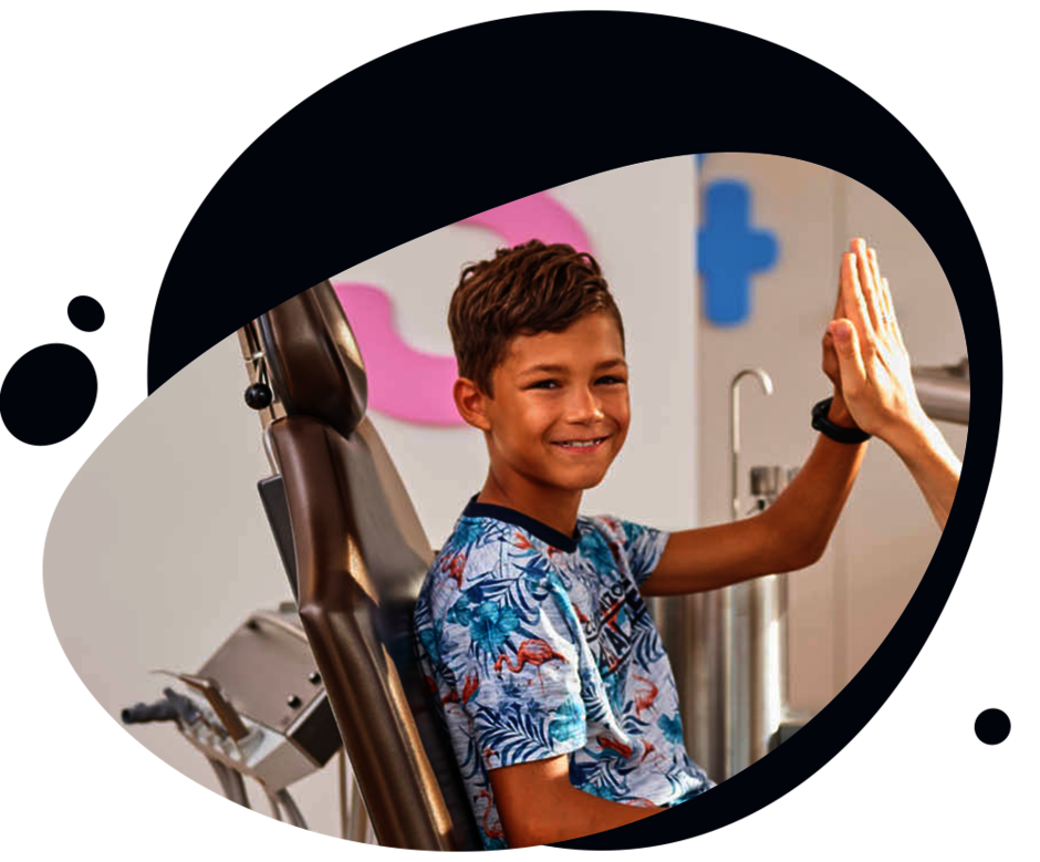 Ein Mädchen unter 6 Jahren sitzt in der kieferorthopädischen Praxis formbar in Forchheim auf einem Kissen und lächelt in die Kamera Ein Junge sitzt im Zahnarztstuhl und gibt Kieferorthopädin Dr. Christina Rathe ein High Five, während er in die Kamera lächelt